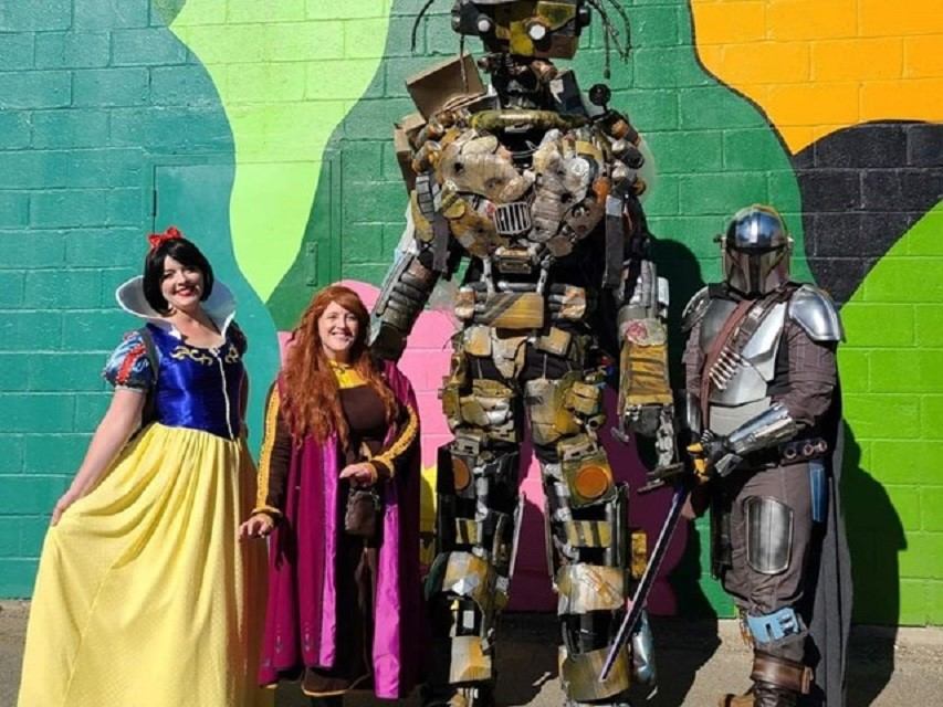 Four cosplayers in bright costumes pose by a colorful mural.