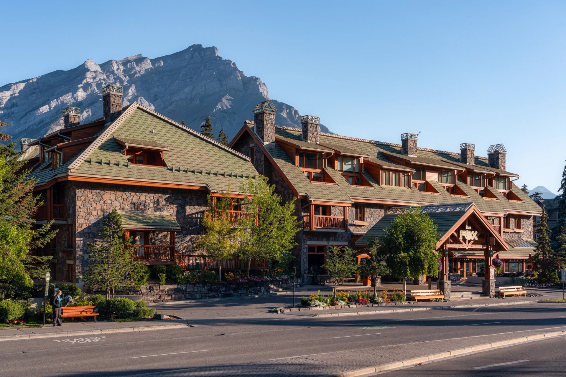 Rustic Fox Hotel with green roofs and mountain backdrop under blue sky.