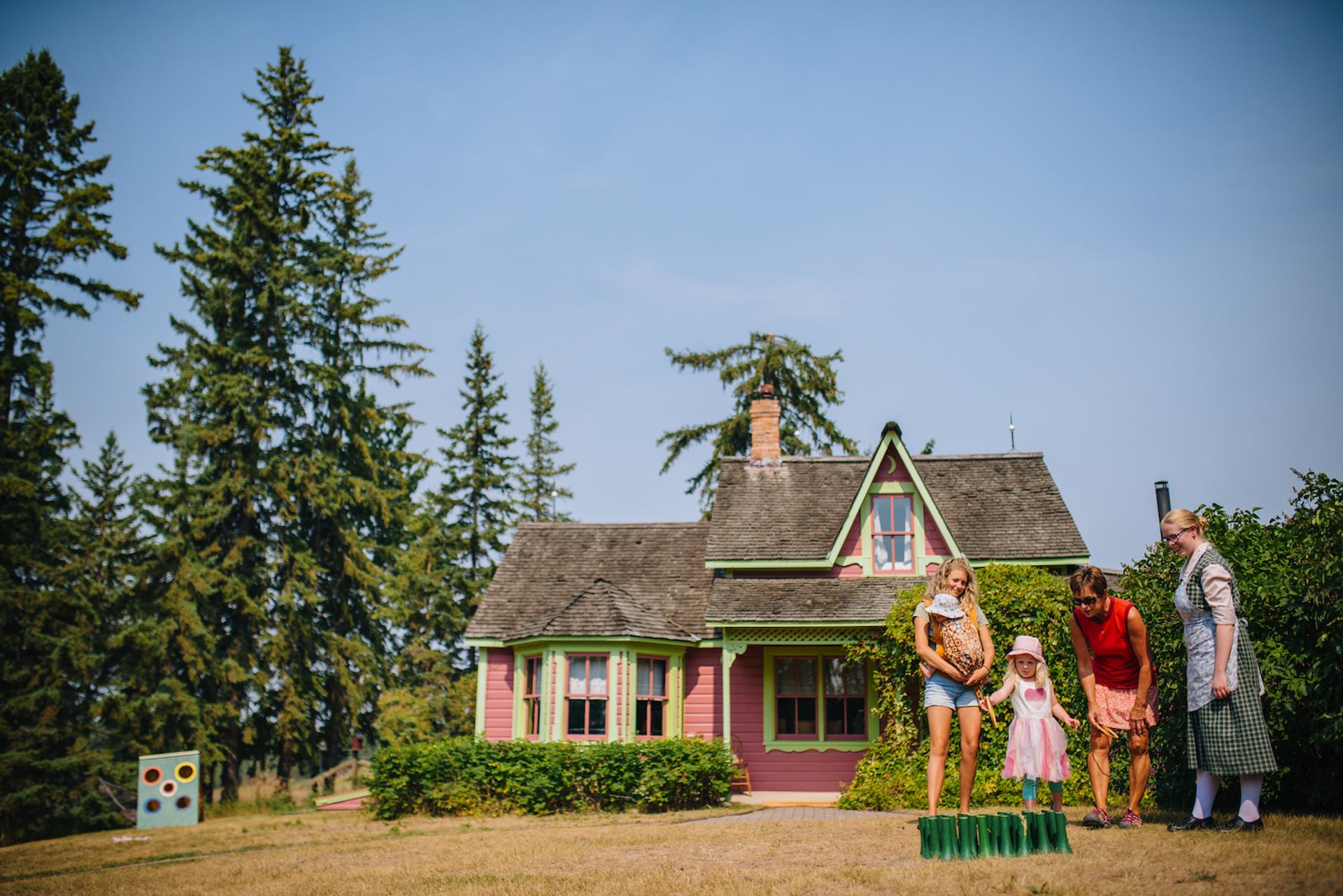 Pink cottage with green trim and four people playing on dry lawn in front.