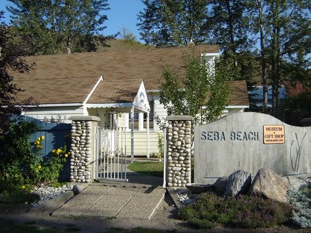 Entrance gate and sign for Seba Beach Museum Gift Shop beside white building.