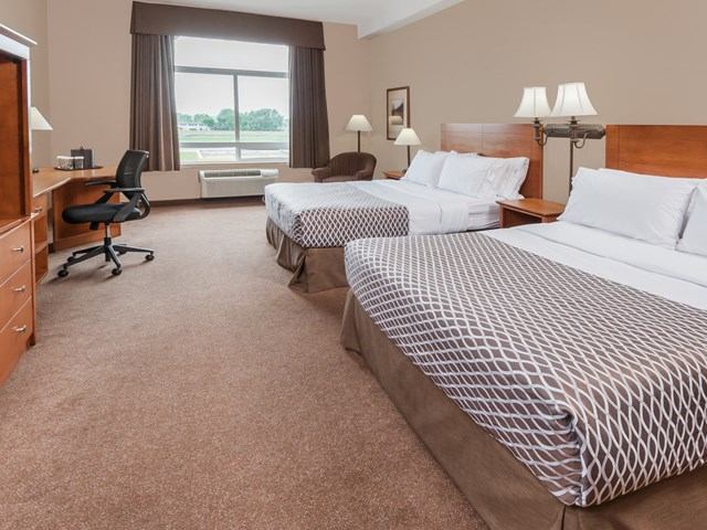 Hotel room at Canalta Airdrie with two beds, desk, TV, armchair, and window view.