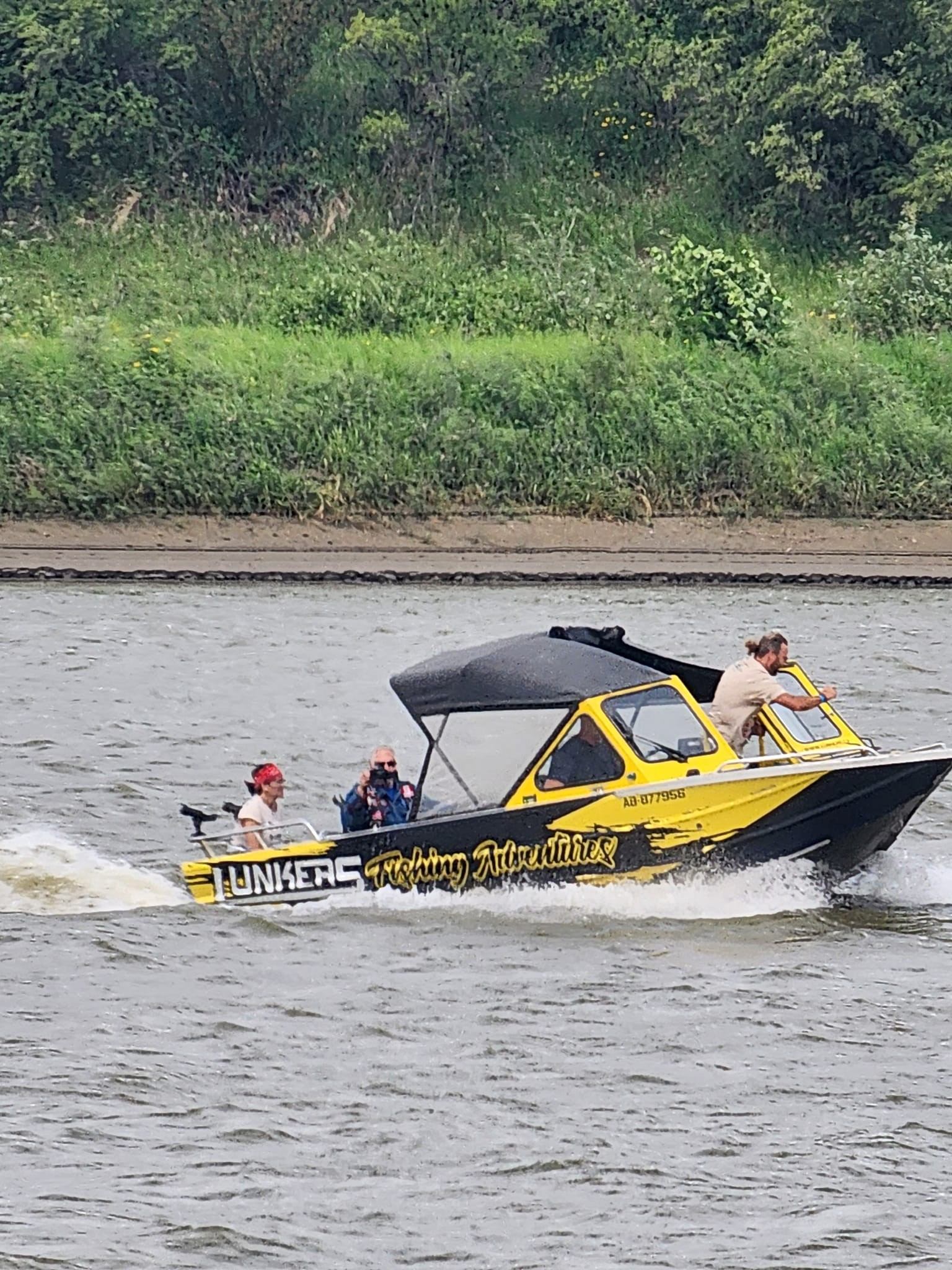 Yellow and black motorboat marked Junkers Fishing Adventures speeds along river.