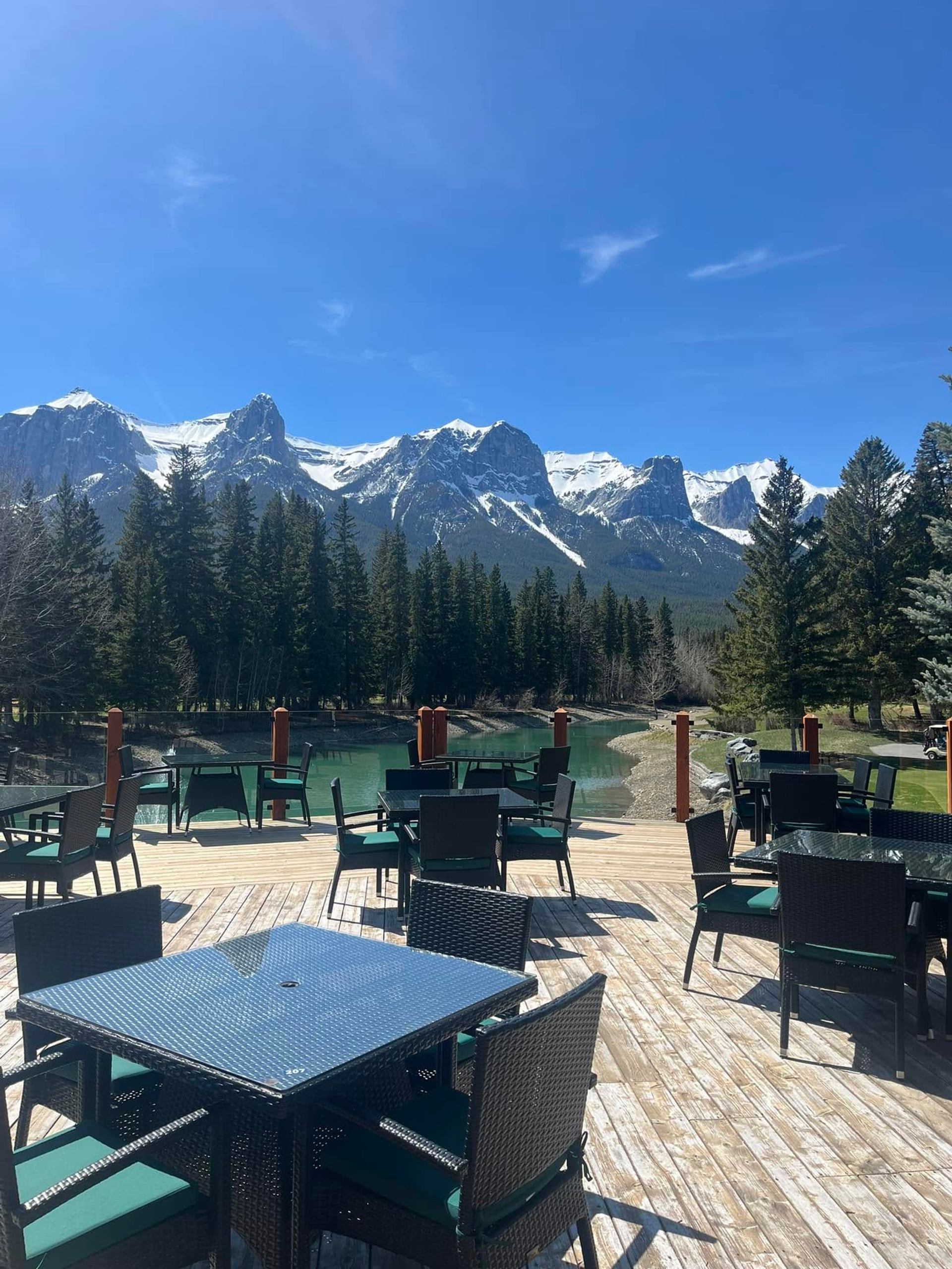 Outdoor restaurant patio with tables overlooking a lake and snowy mountains.