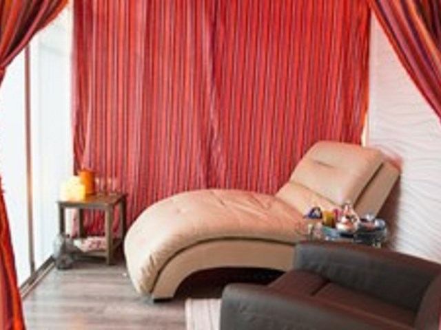 Cozy spa lounge with chaise, candles, red curtains, and textured white wall.