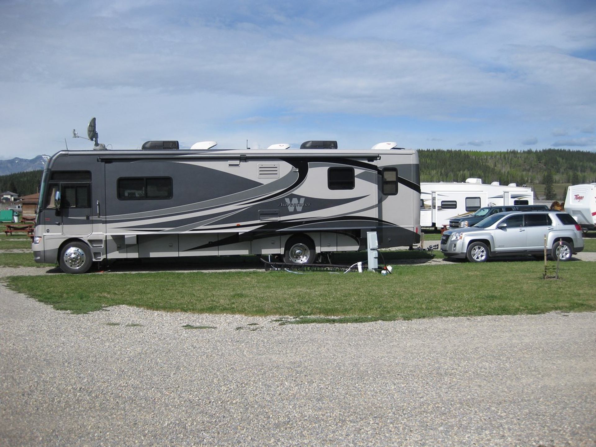 Large motorhome and SUV are parked at a serviced RV campsite with grassy grounds and nearby RVs.