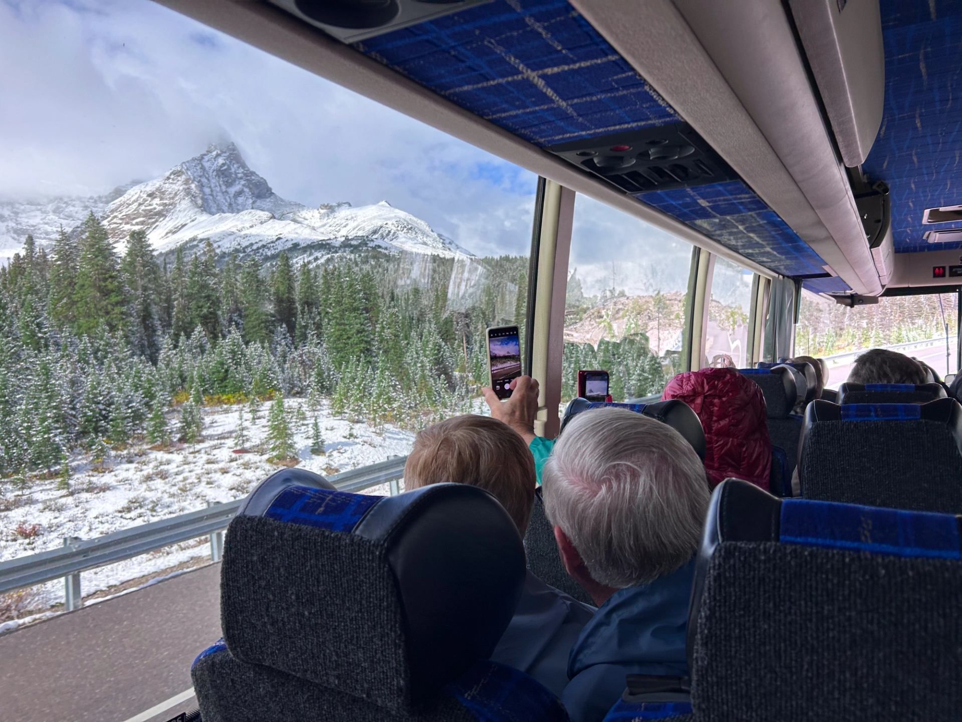 Passengers photographing snowy mountain scenery through bus windows.
