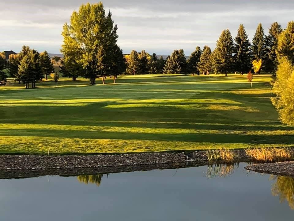 Golf course green with trees and a small pond in the foreground, Alberta.