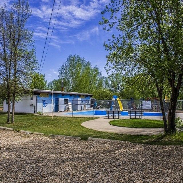 Fenced outdoor pool with yellow slide beside low building and trees.