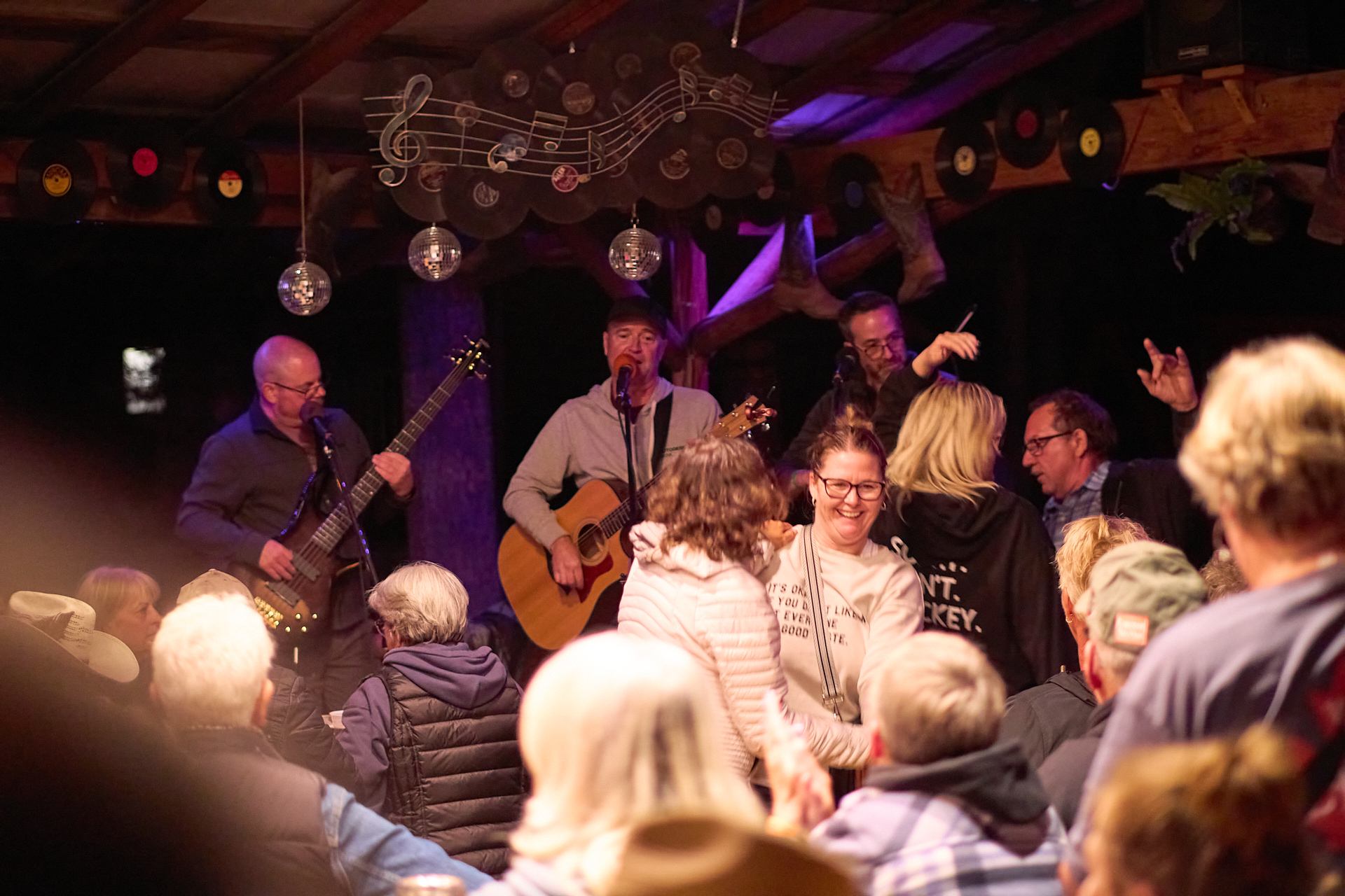 Musicians perform with guitars as a crowd gathers near the stage.