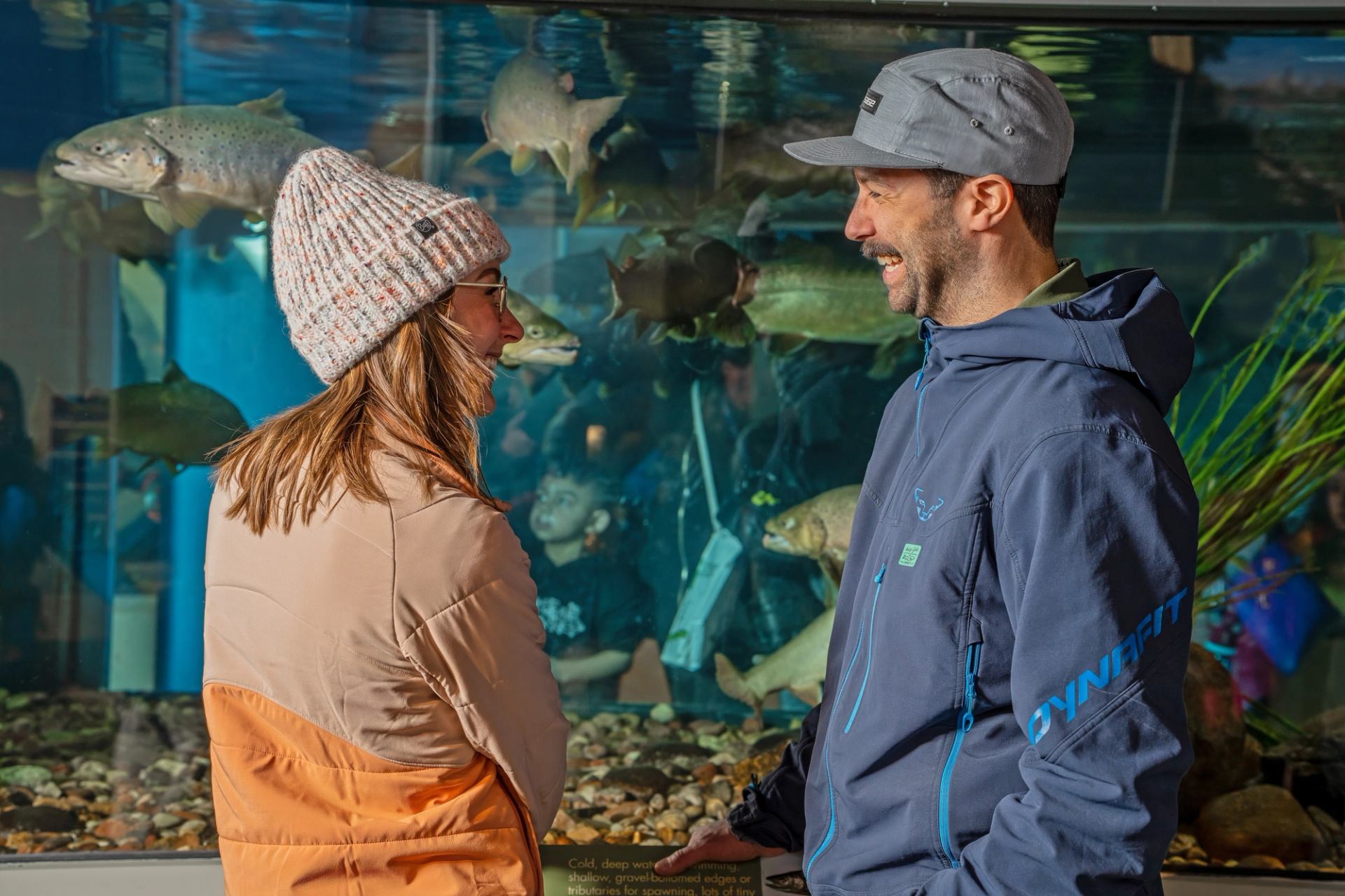 Two people viewing fish in a large aquarium at Fishtival, surrounded by aquatic plants and clear water.