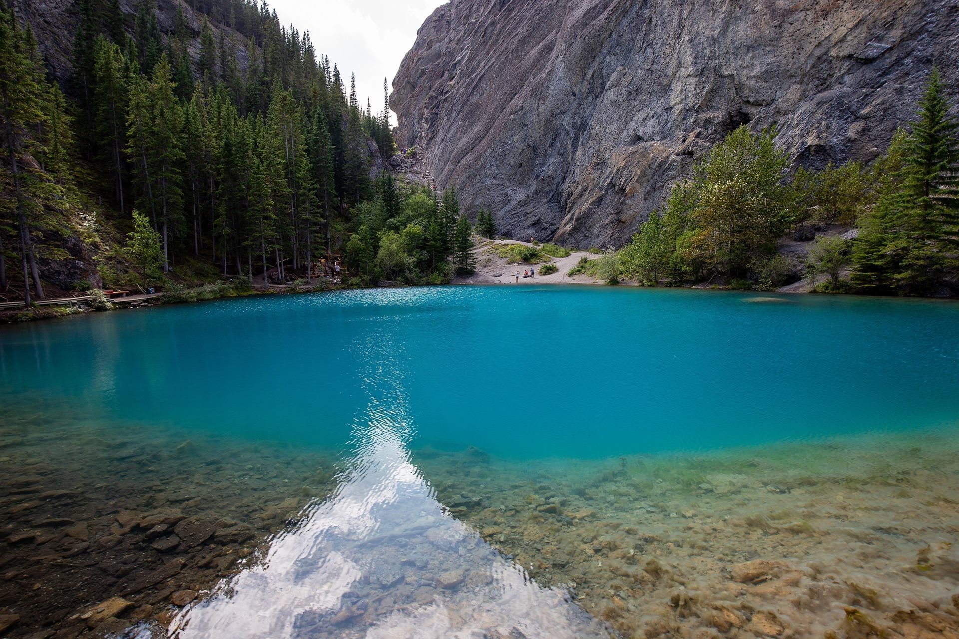 Turquoise mountain lake with rocky shoreline, surrounded by dense evergreen forest and cliffs.