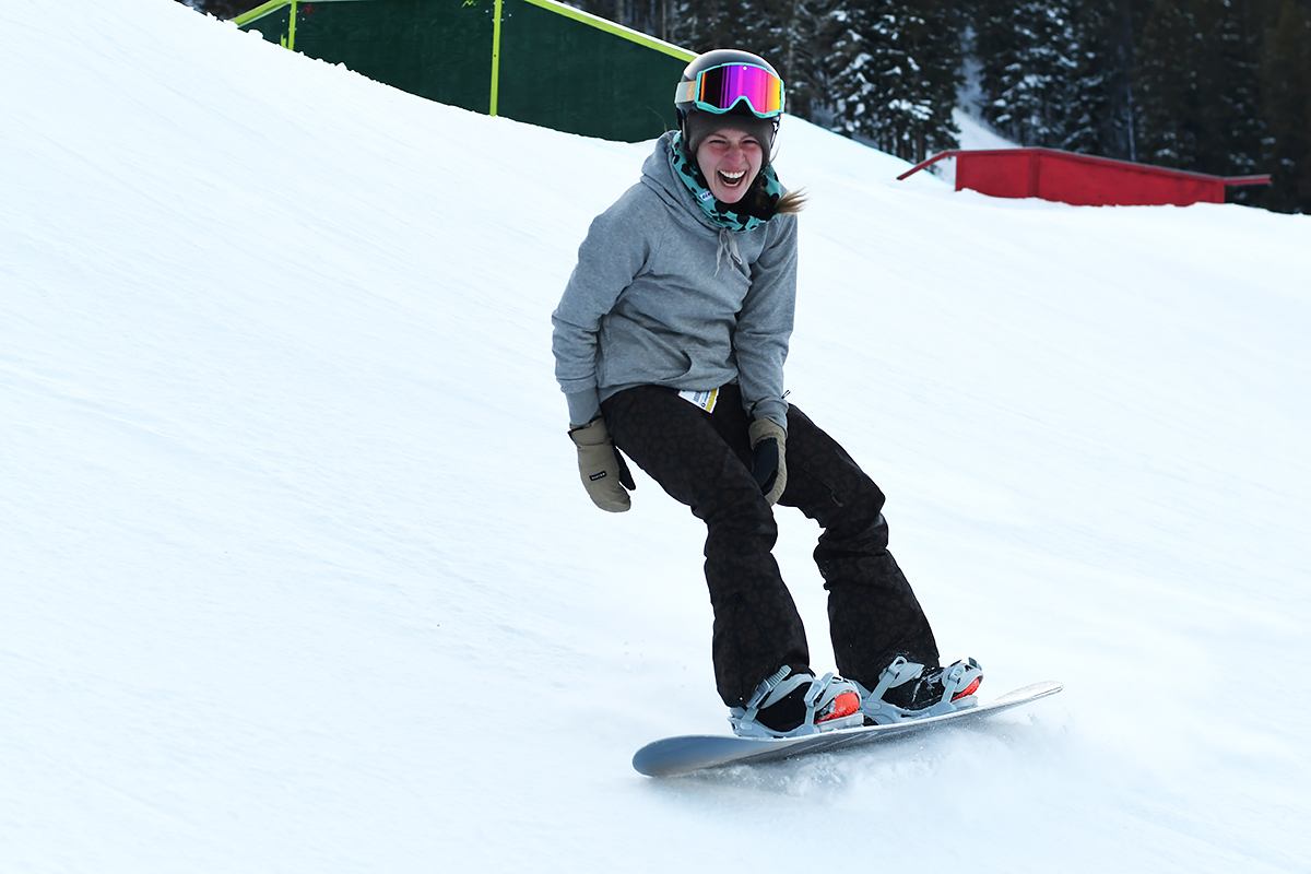 A smiling snowboarder glides down a snowy slope.