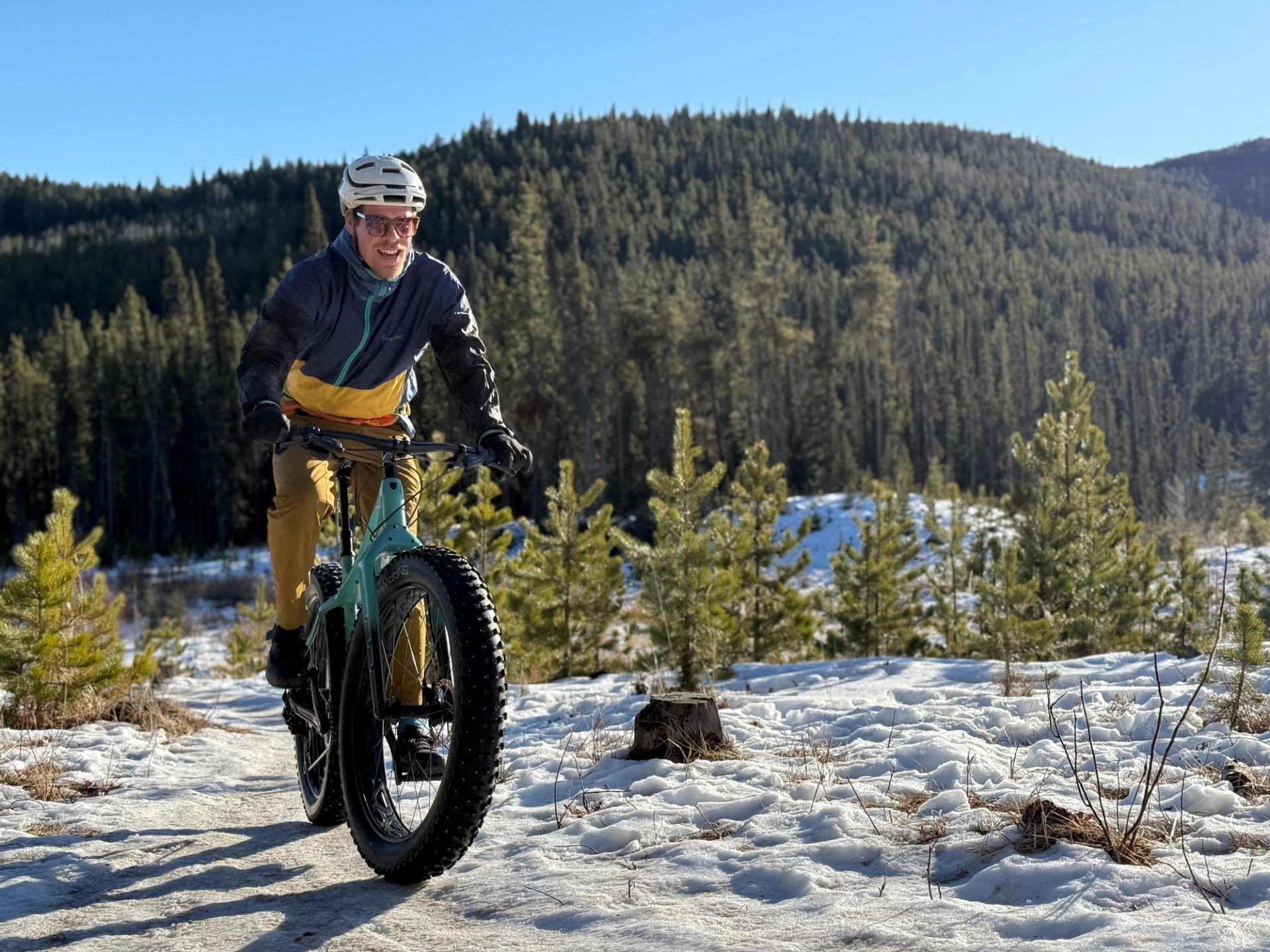 Mountain biker on snowy trail with forested hills in background, Foothills, Alberta.
