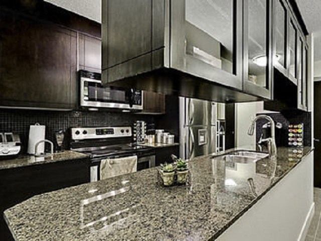 Modern kitchen with granite counters, stainless steel appliances, and dark cabinets at Corporate Suites of Calgary.