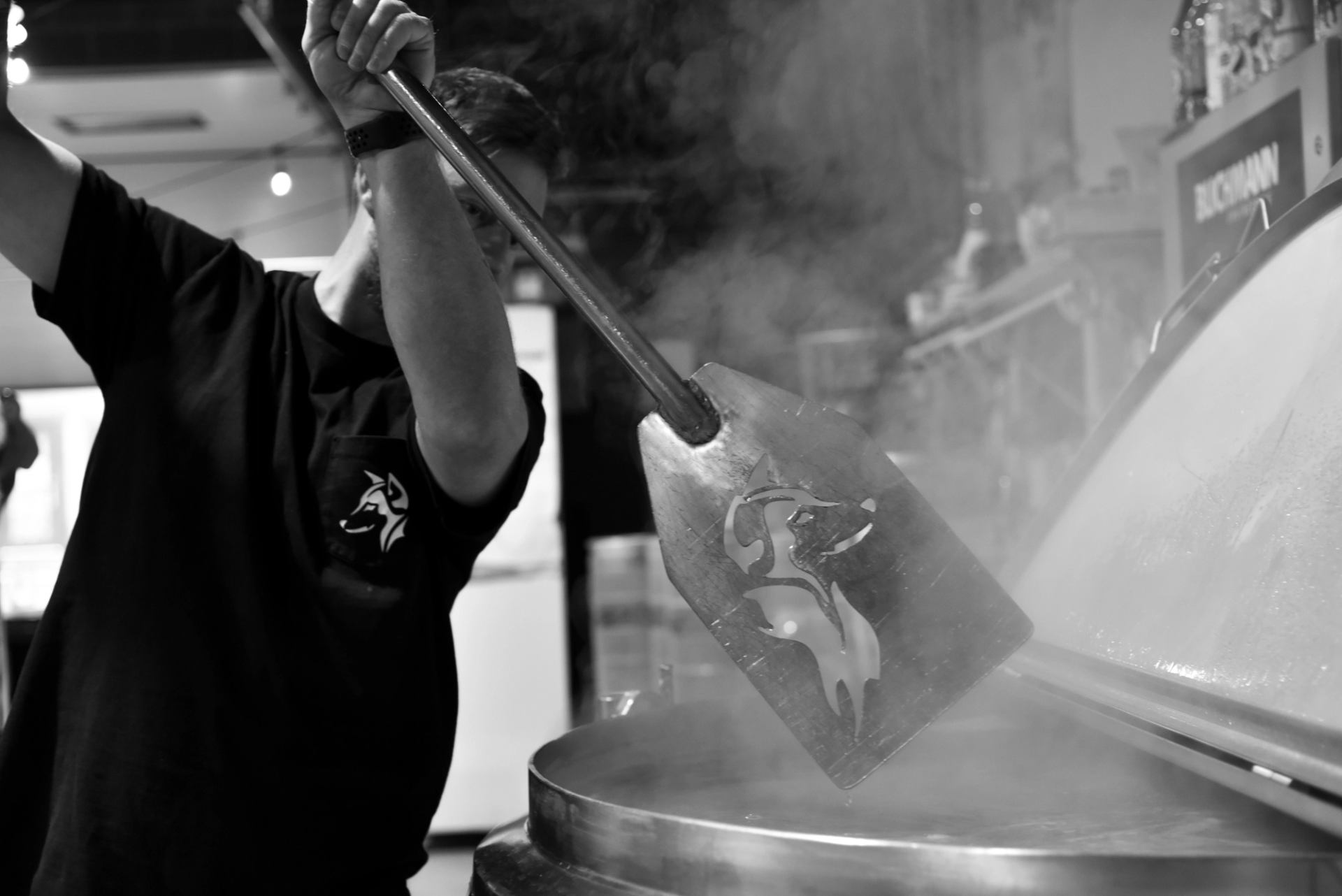 Worker stirs a steaming industrial vat with a long metal paddle.