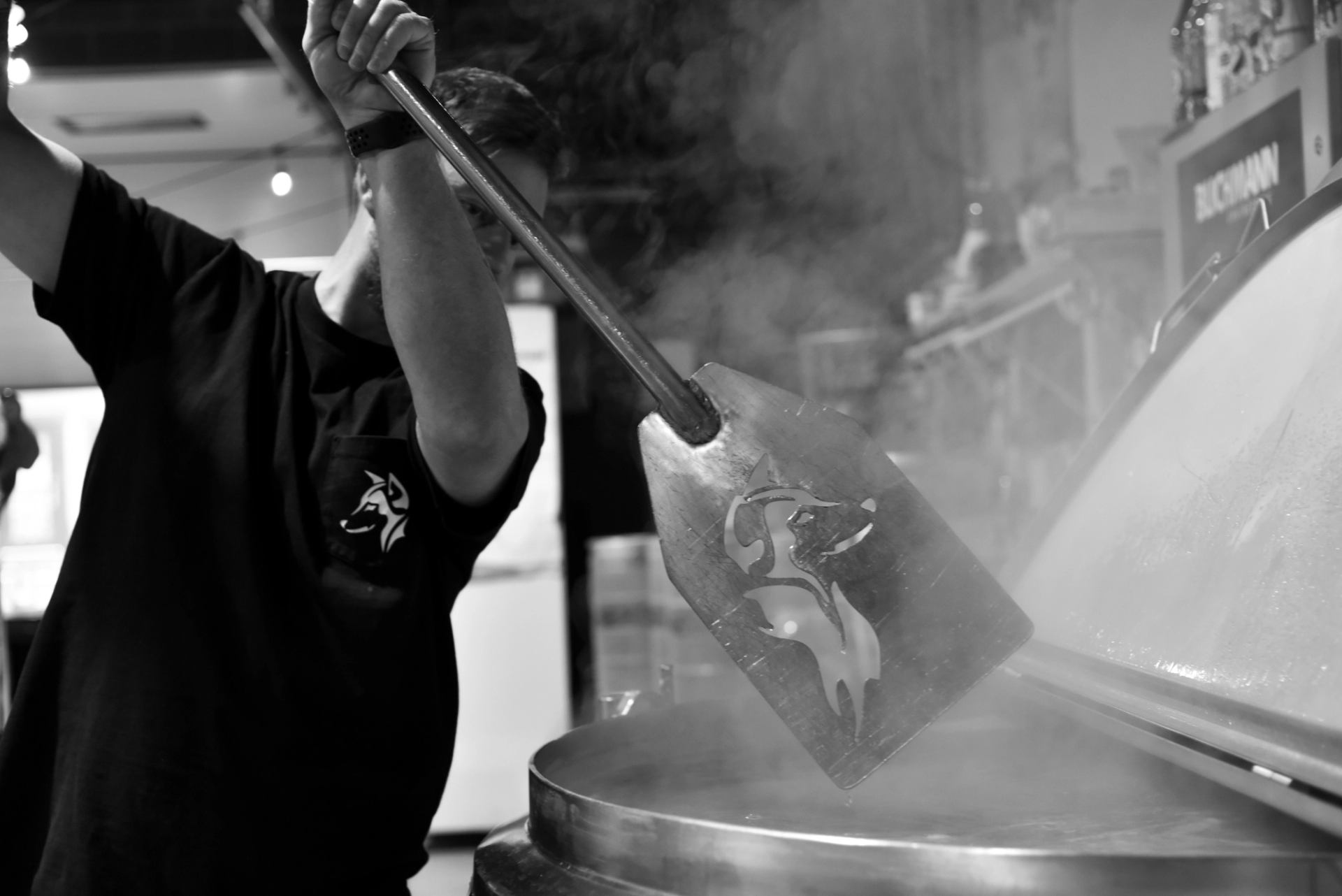 Worker stirs a steaming industrial vat with a long metal paddle.