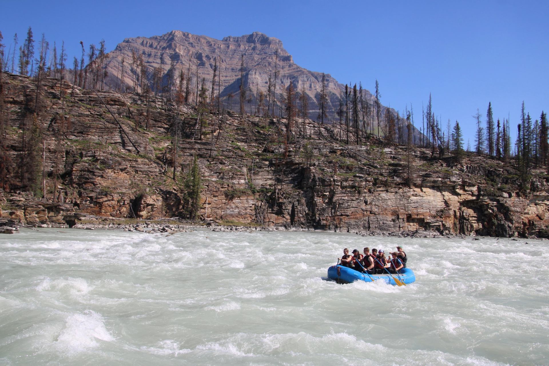 Rafting group navigating fast-moving river with rocky cliffs and a mountain backdrop.