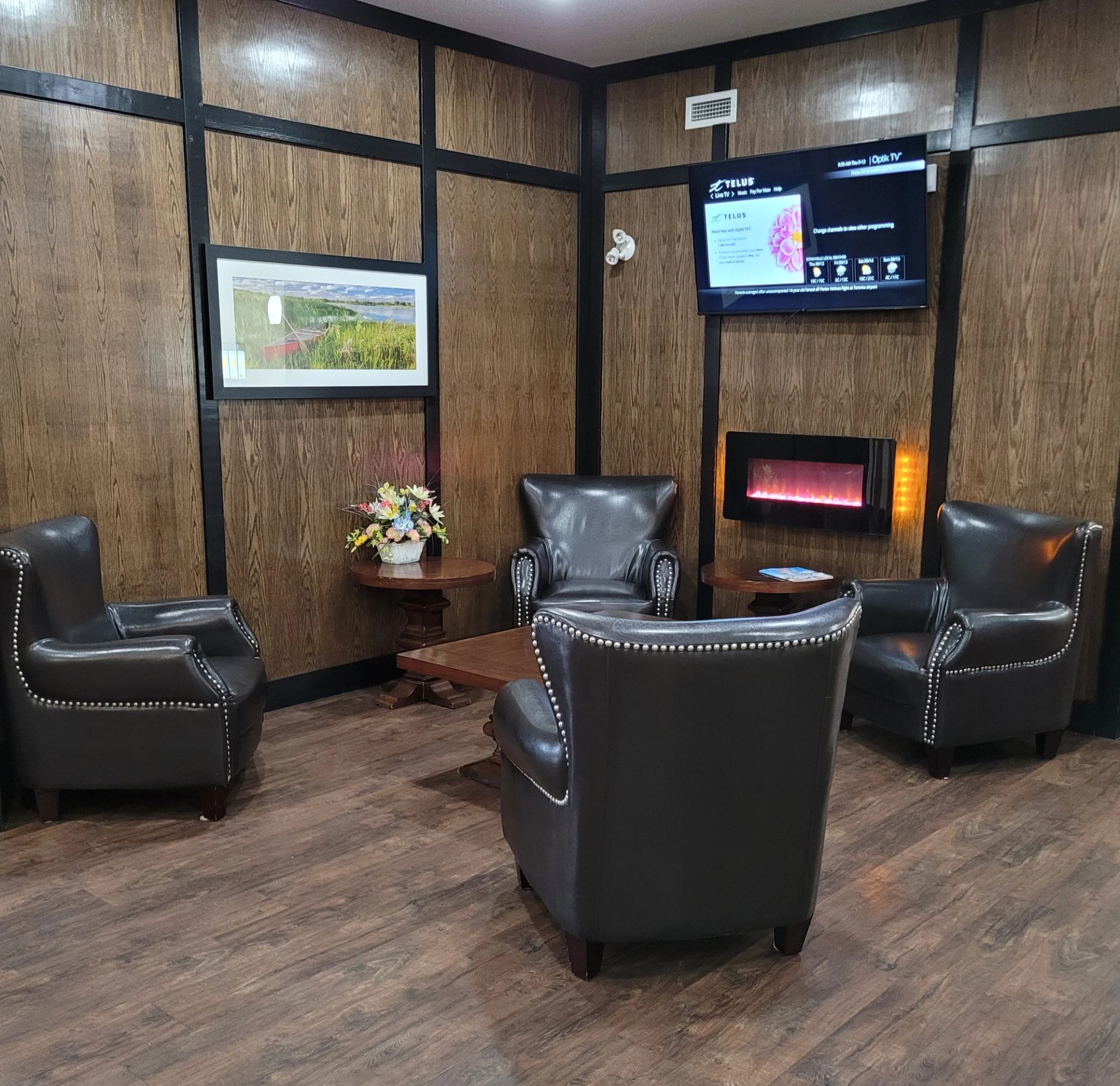 Hotel lounge area with black leather chairs, wooden walls, flat-screen TV, and fireplace.