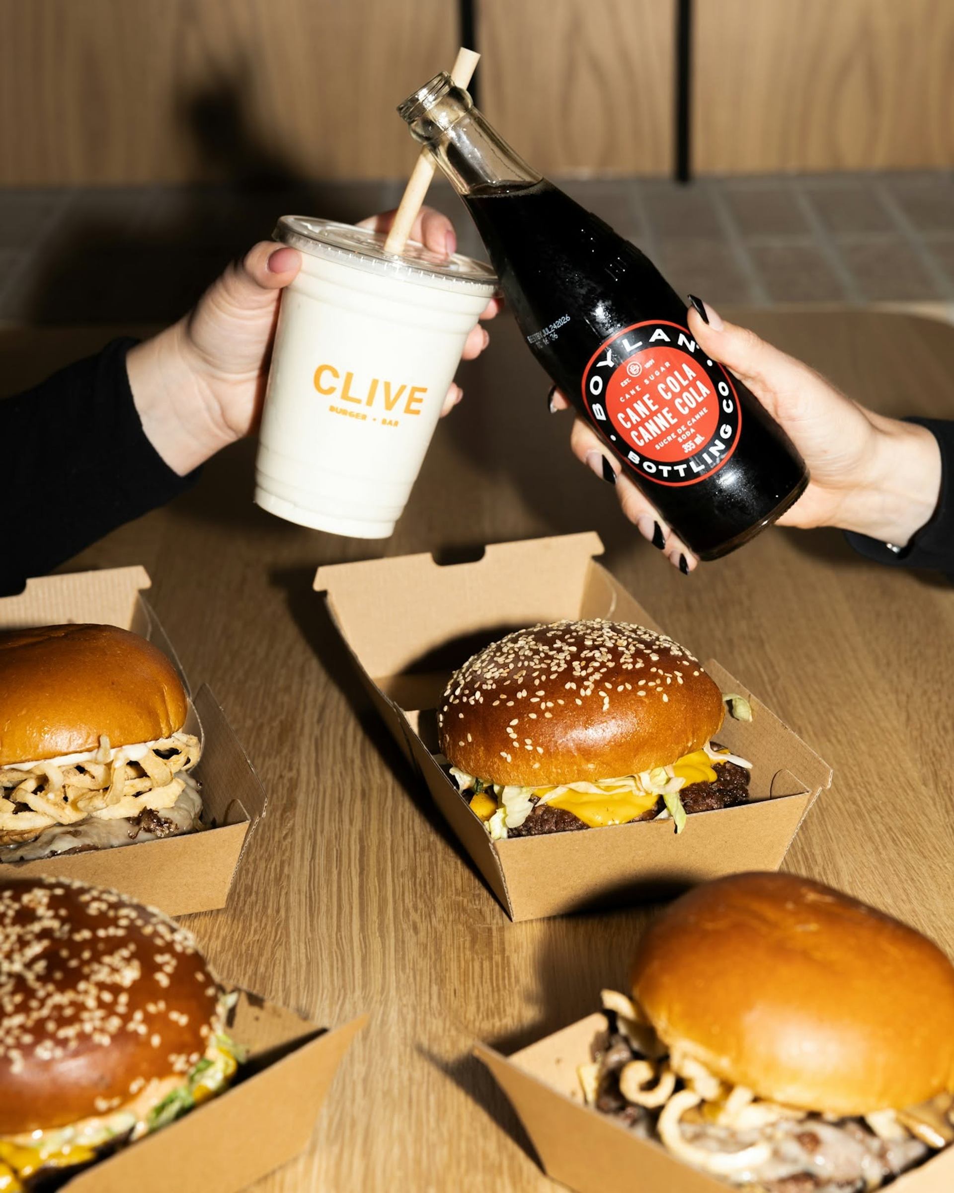 Burgers, a milkshake, and bottled soda are served on a table inside Clive Burger.