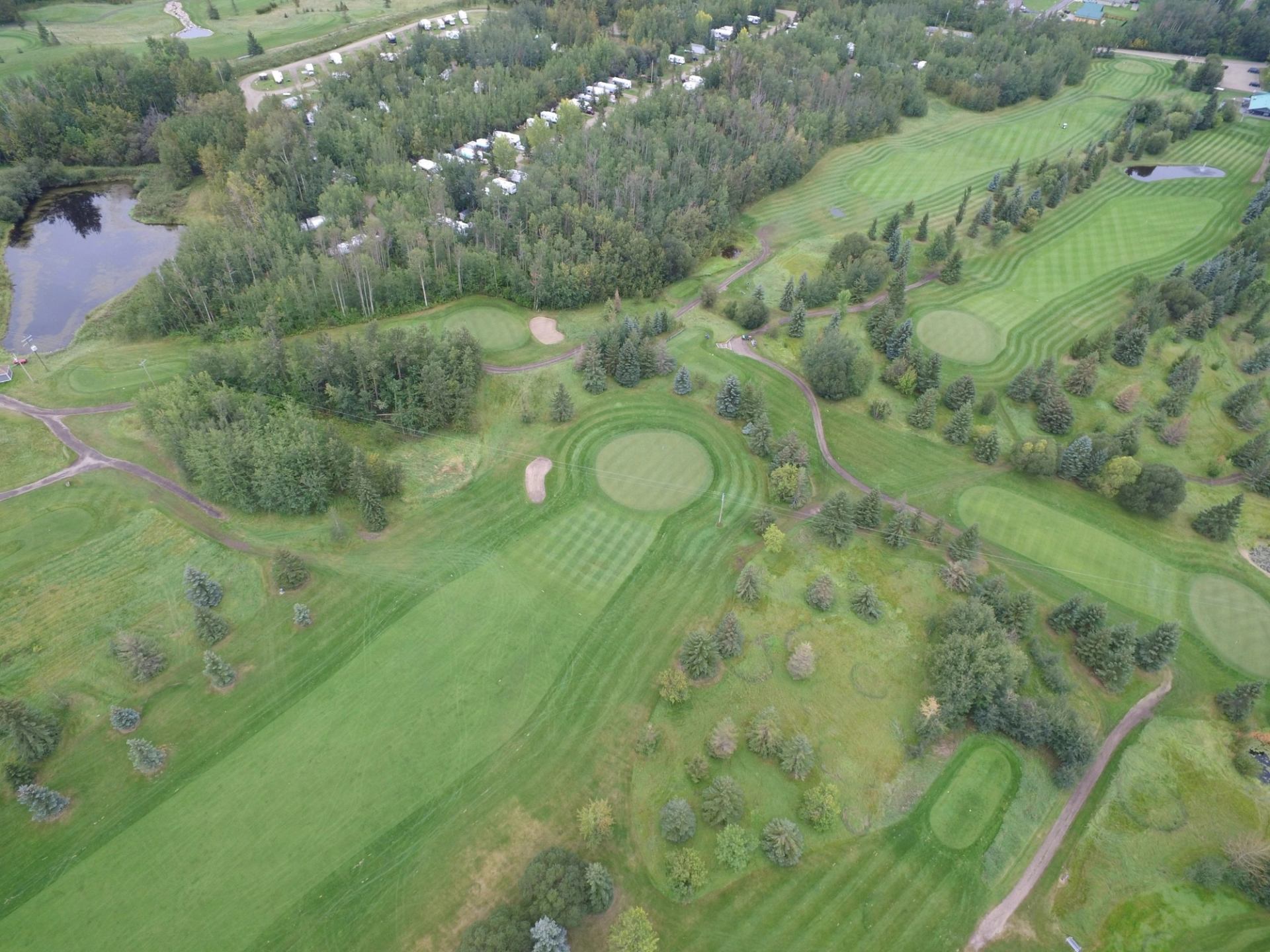 Aerial view of a golf course with greens, fairways, trees and nearby campground.