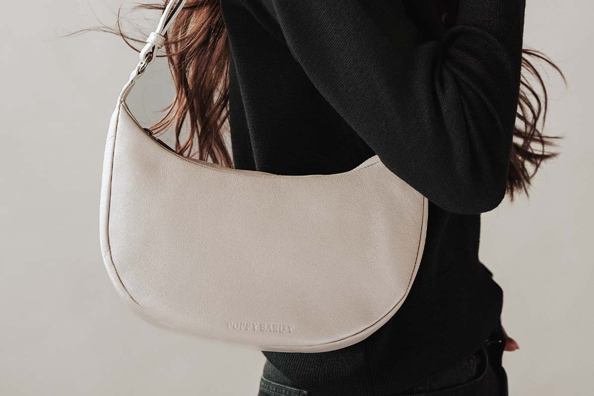 Crescent-shaped light handbag over shoulder, worn with black long-sleeved top.