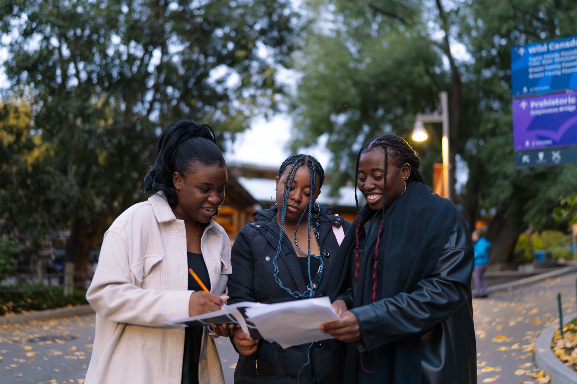 Three people review papers together on a tree-lined path.