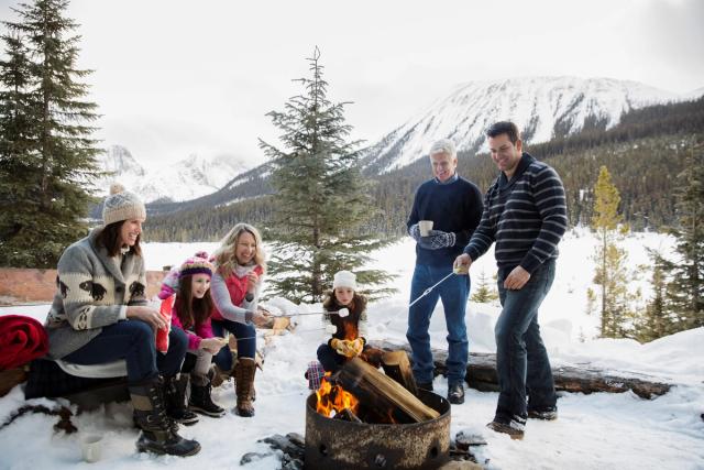 Family and friends roasting marshmallows over a campfire at Mount Engadine Lodge in Kananaskis Country.