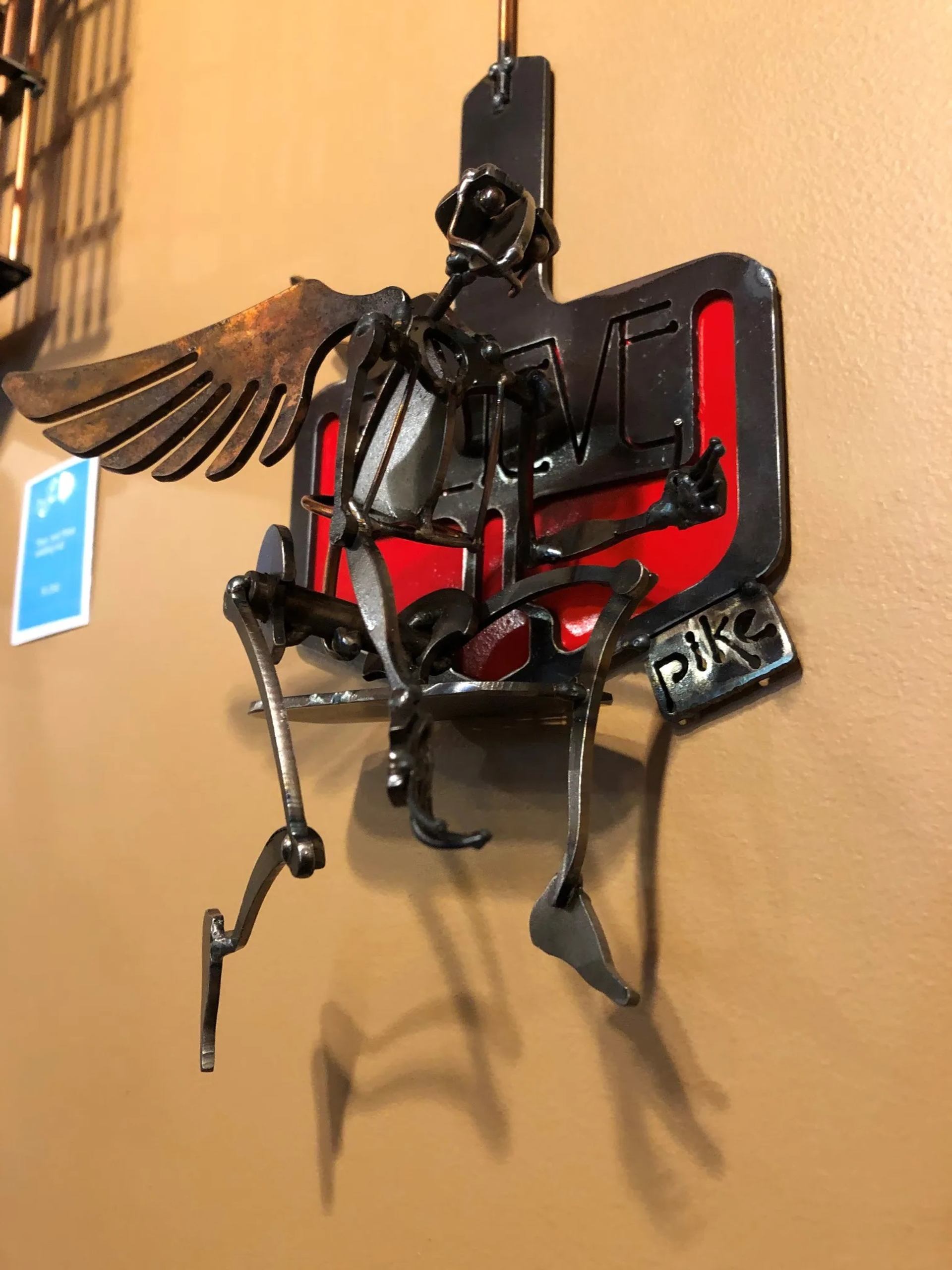 Metal sculpture of a winged figure mounted on a red and black base at Pike Studios.