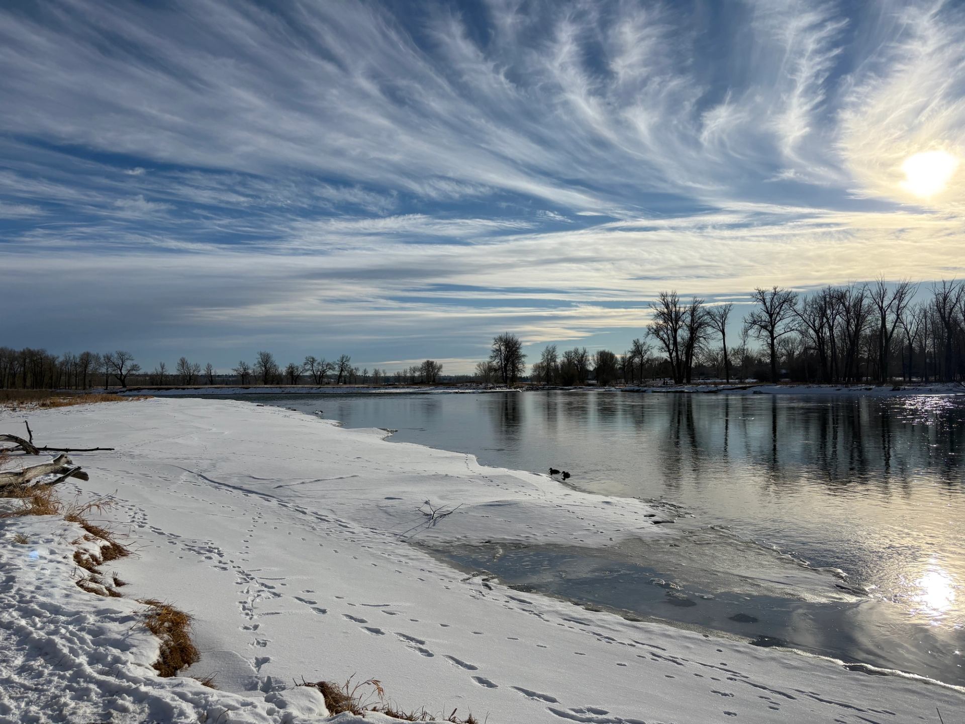 Partially frozen river with snowy banks under dramatic winter skies.