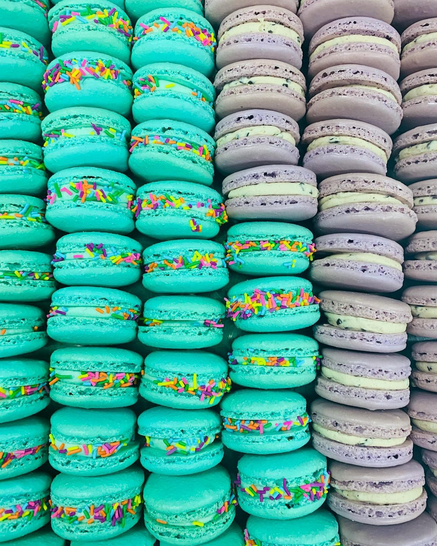 Stacks of turquoise macarons with rainbow sprinkles beside lavender macarons with cream filling.