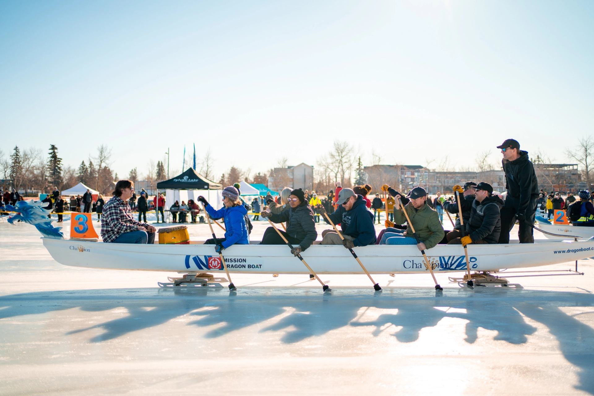 Dragon boat race on ice with participants holding paddles at Sylvan Lake festival.