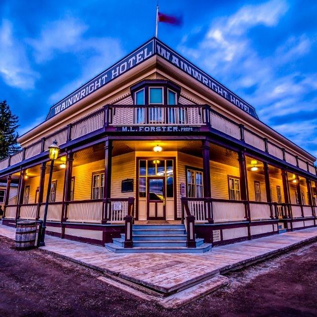 Cariboo Wright Hotel exterior with wraparound veranda, illuminated lamps and rooftop flag.