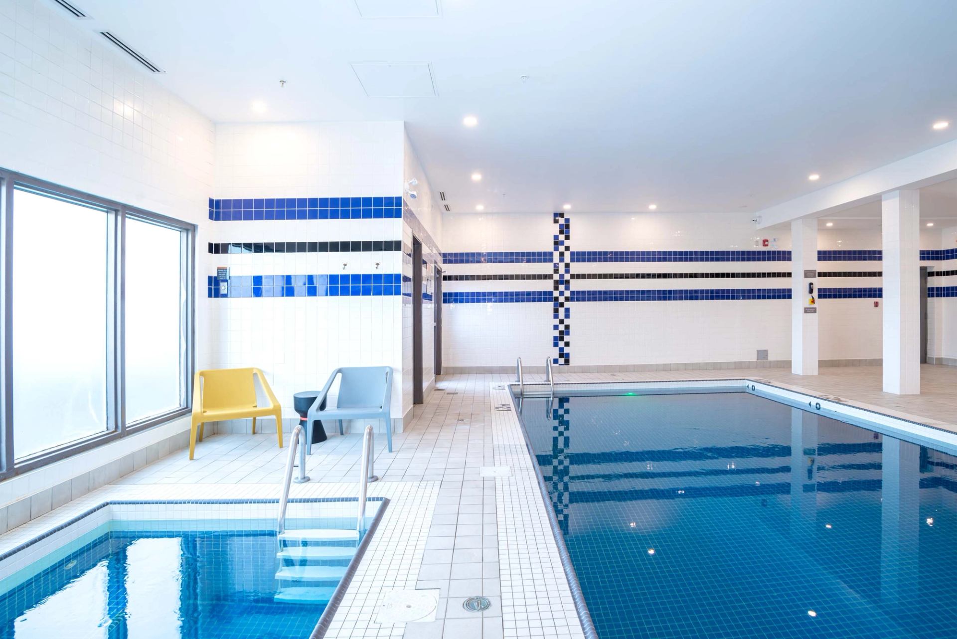 Indoor swimming pool and hot tub with tiled deck and colourful plastic chairs.