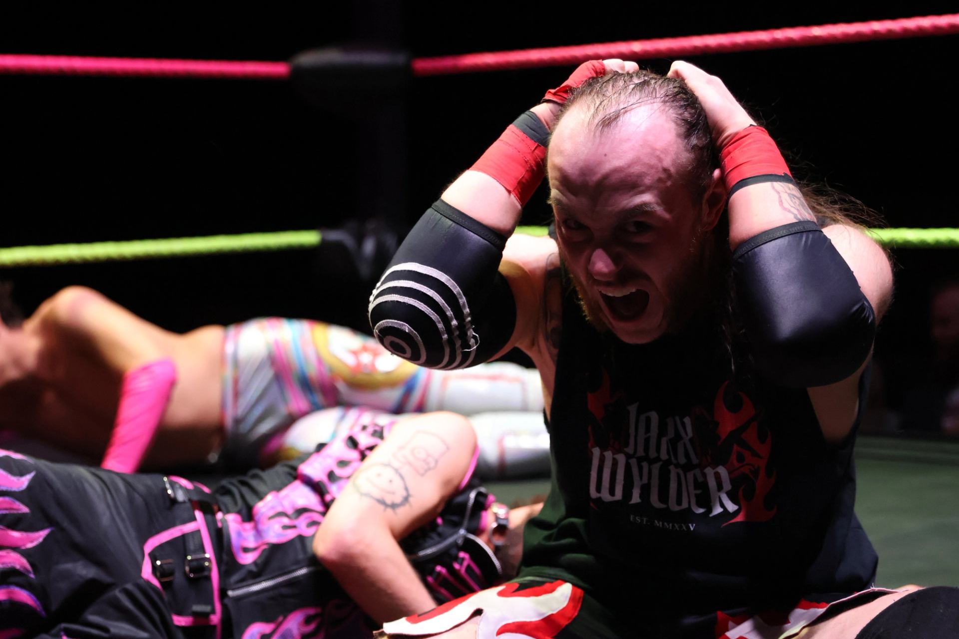 Wrestler seated in the ring holding their head while other competitors lie nearby.