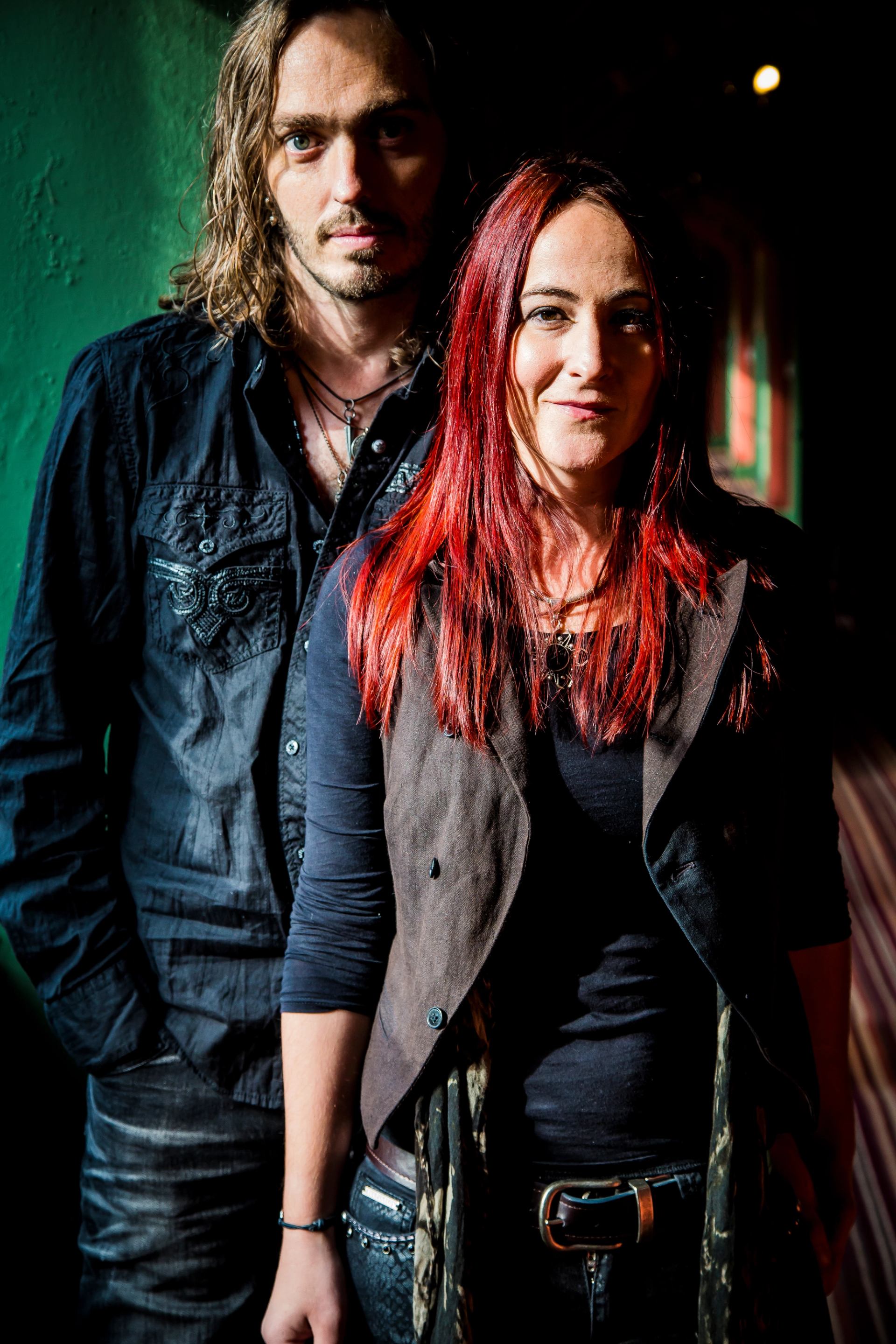 Two people in dark clothing stand indoors, lit by strong side light.
