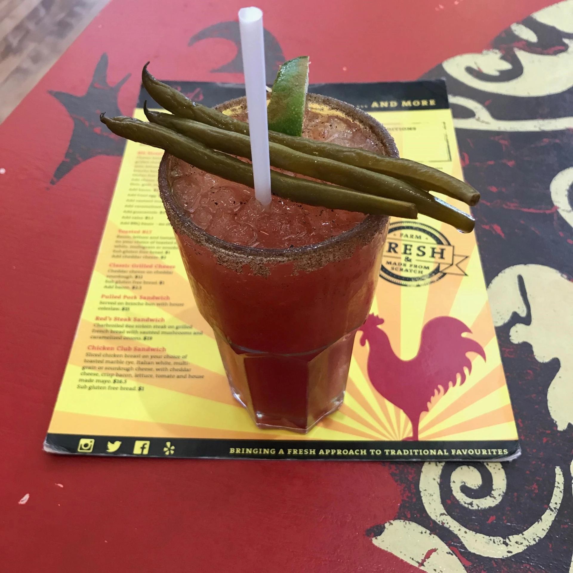 Bloody Mary cocktail garnished with green beans and a straw on a menu.