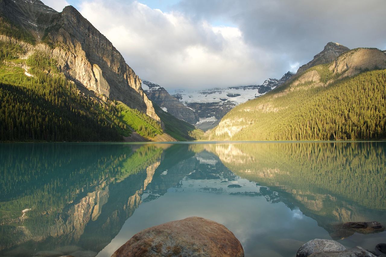 Turquoise mountain lake with rocky shore, forested slopes and distant snow-covered peaks.