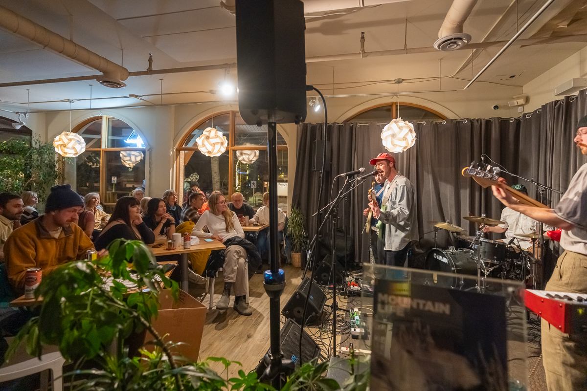 Band performing indoors as the audience listens from tables in a warm, relaxed setting.