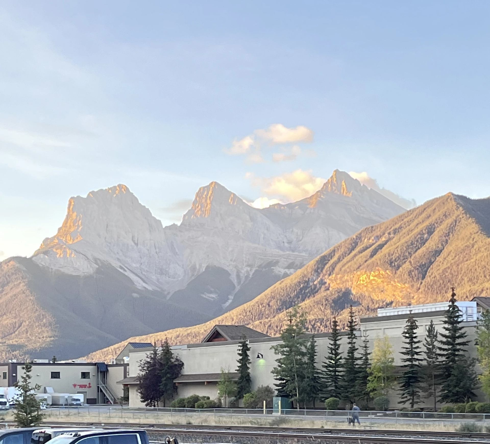 Rocky mountain peaks behind small town buildings, evergreen trees and railway tracks.