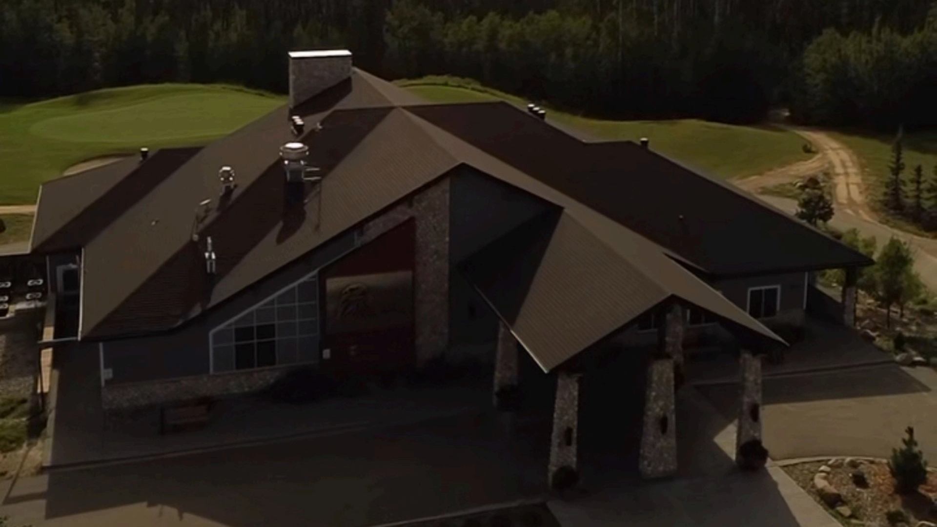 Large lodge with angular brown roofs, stone pillars and surrounding green hills.