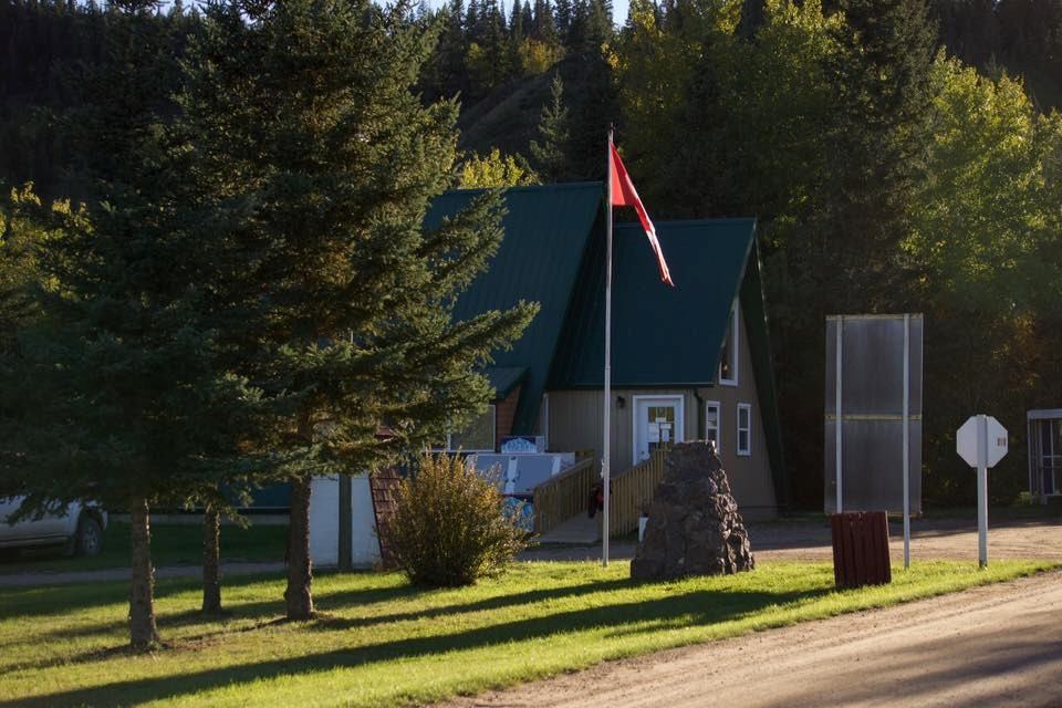 Small green-roofed building with flagpole and monument in a wooded park setting.