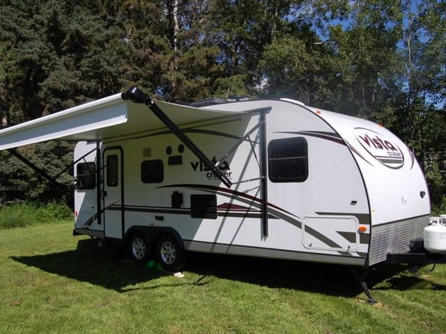 White Vibe travel trailer with awning parked on grass, ready for camping.