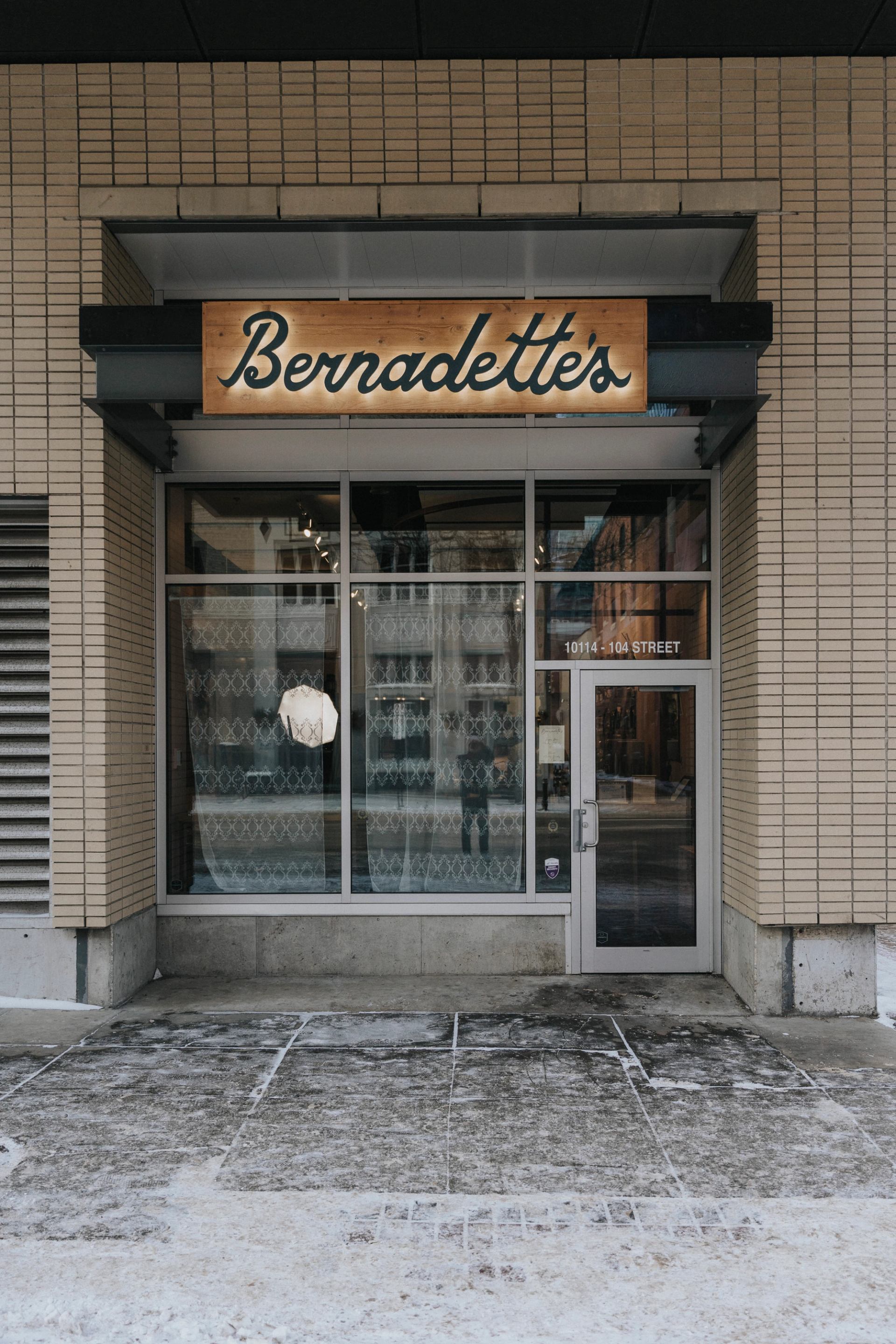 Storefront with Bernadette’s sign, glass door, patterned window coverings and snowy sidewalk.