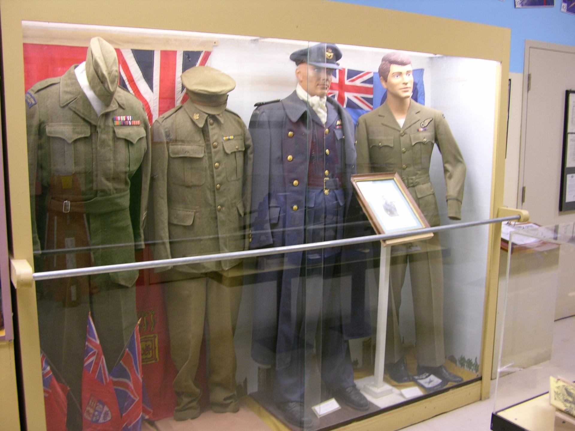 Display case with historic military uniforms, hats, and flags inside a local museum.