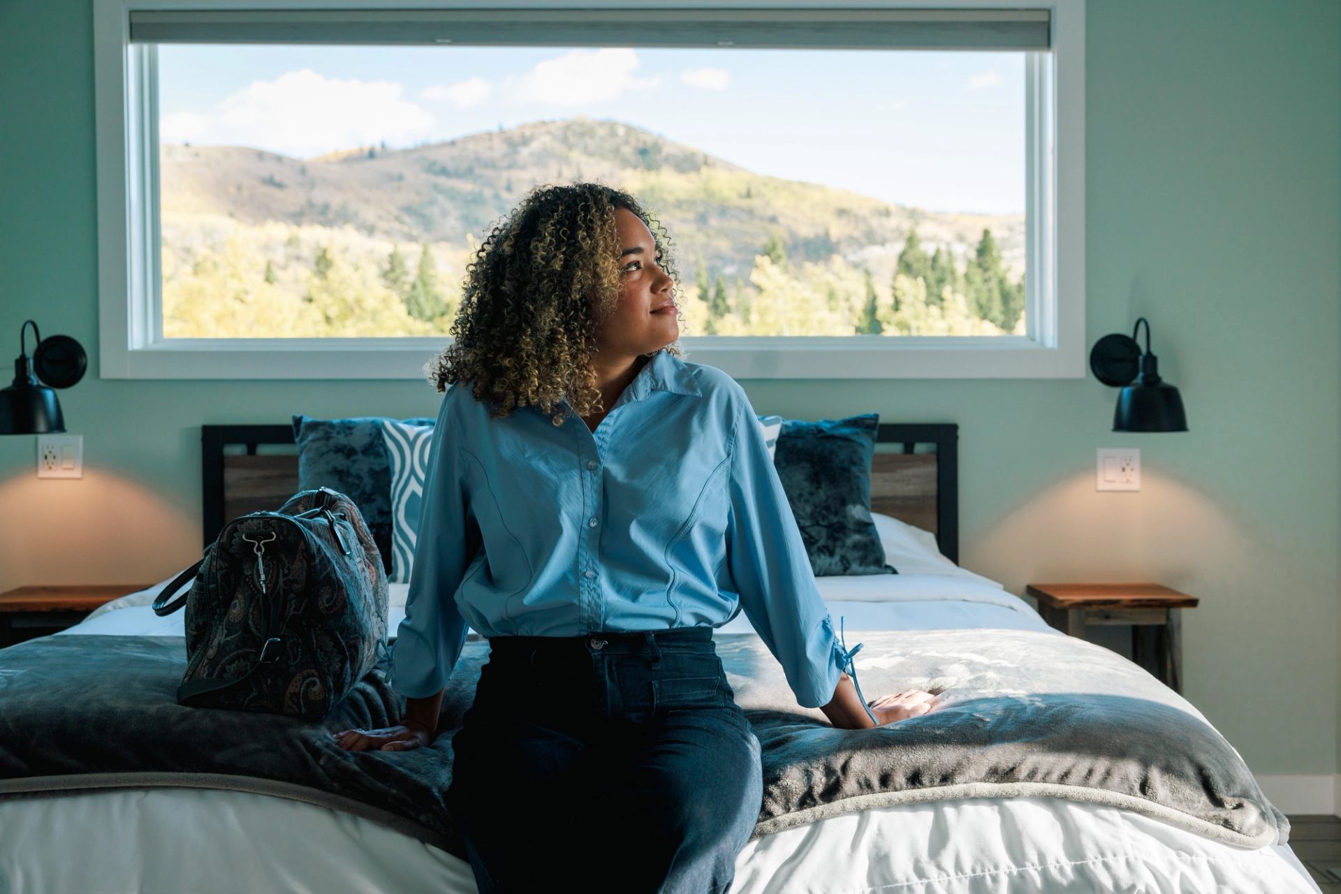 Guest seated on bed, gazing at mountain view at River Retreat Kananaskis.