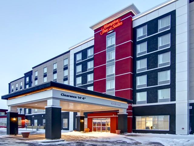 Exterior of Hampton Inn Grande Prairie with red and gray facade, covered entrance, and snow.