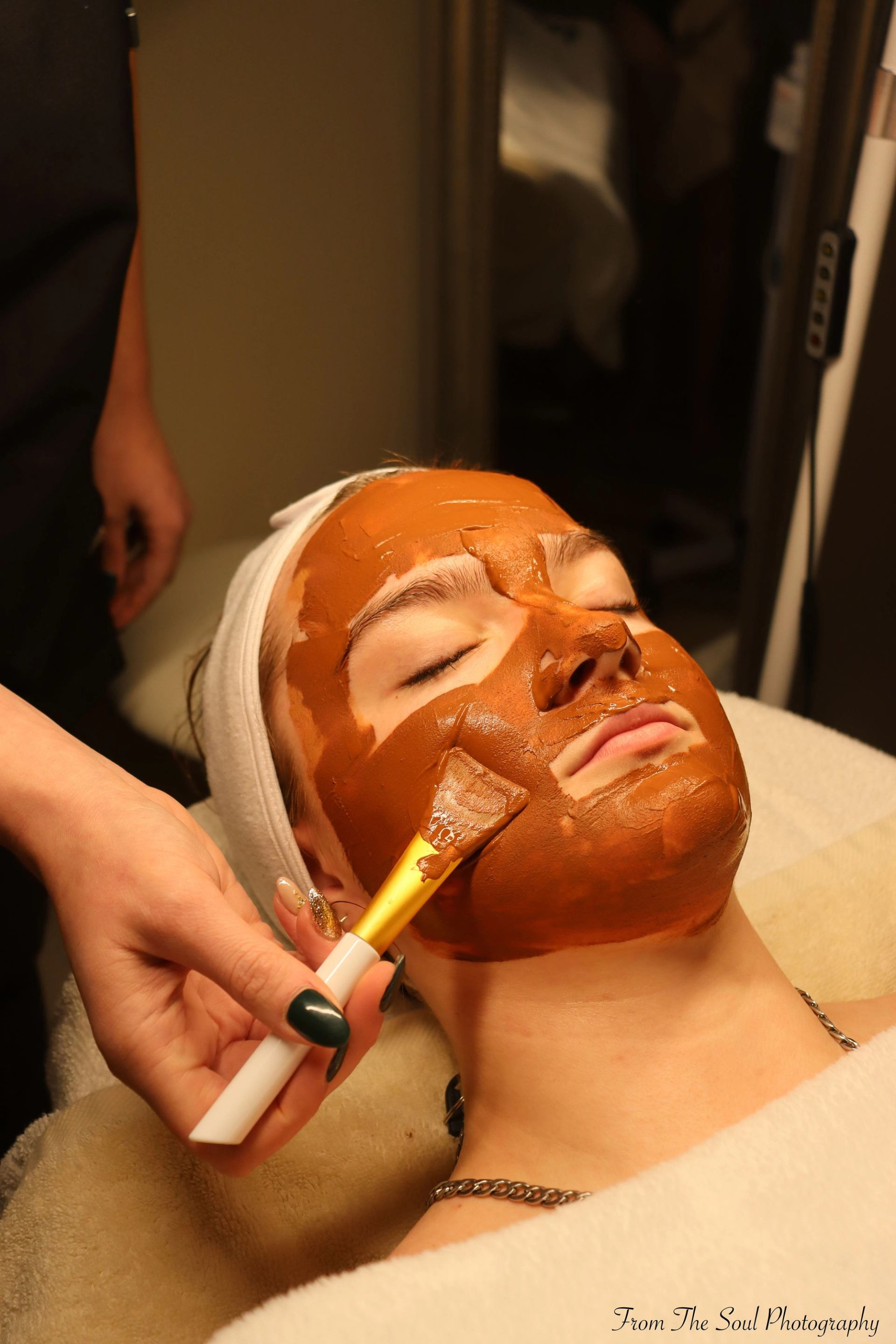 Spa facial treatment with brush-applied mask and towel-wrapped head.