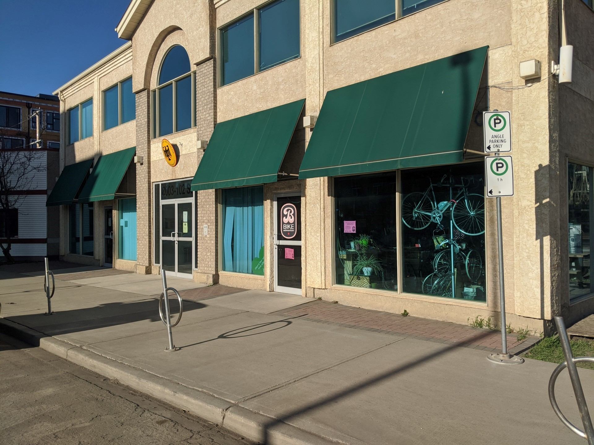 Beige building with green awnings and a bike rack on the sidewalk.