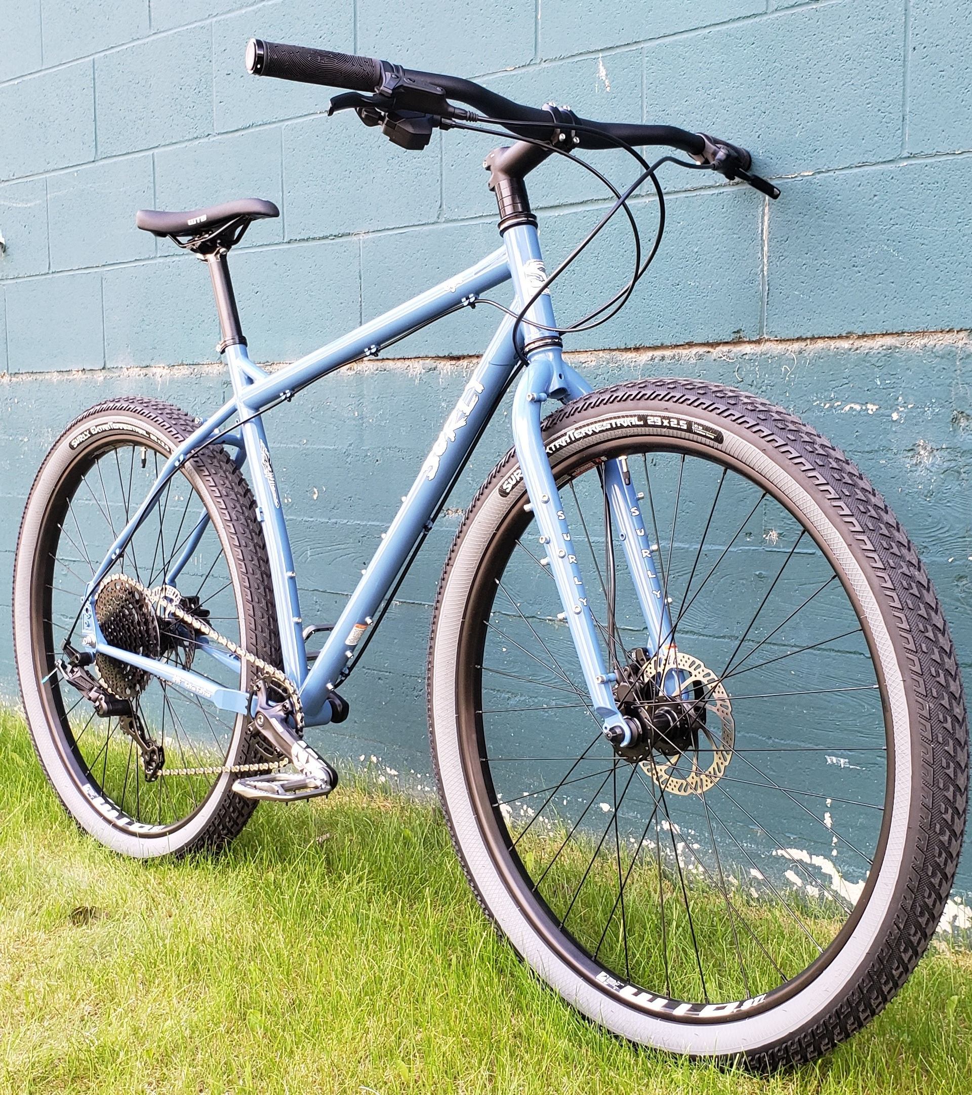 Blue bike with black tires leaning on teal brick wall over grass.