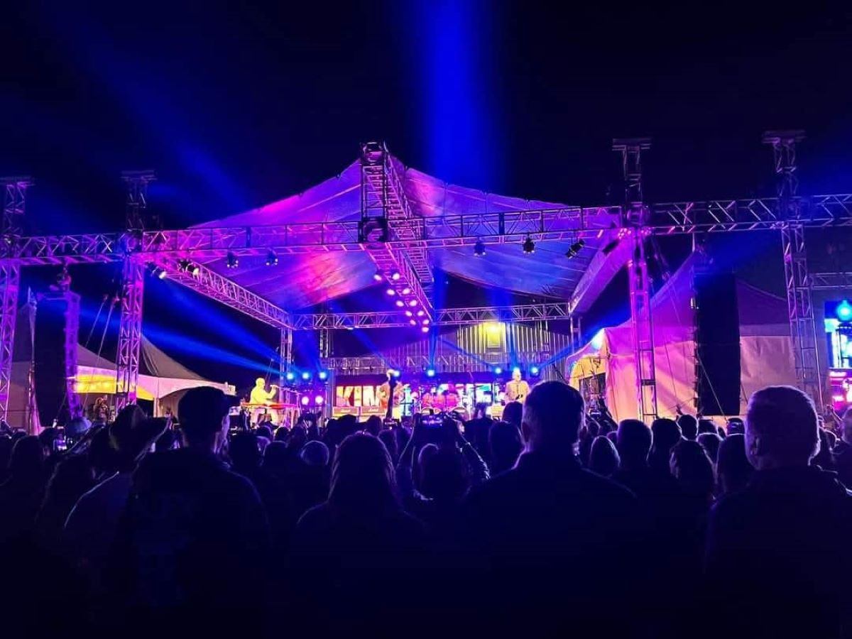 Outdoor concert stage with colourful lights shining over a large standing crowd at night.
